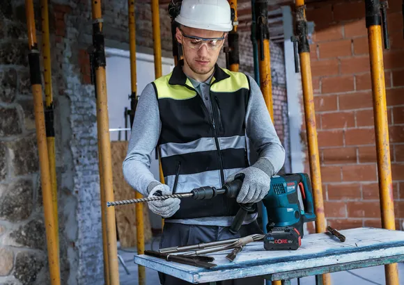 Una persona que usa equipo de seguridad coloca una broca en un martillo perforador en un sitio de construcción.