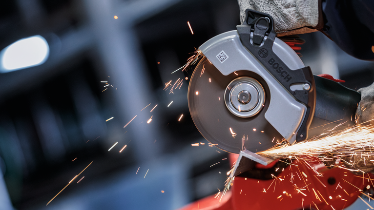 Una persona que usa equipo de seguridad muele metal, produciendo chispas brillantes.