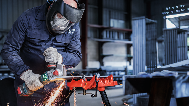 Una persona que usa equipo de seguridad utiliza una herramienta eléctrica para moler metal y crear chispas.