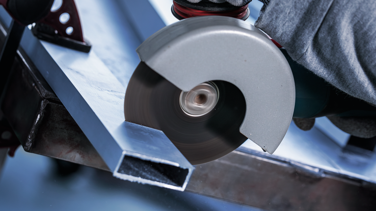 Una persona que usa equipo de seguridad corta una viga de metal con una amoladora angular.