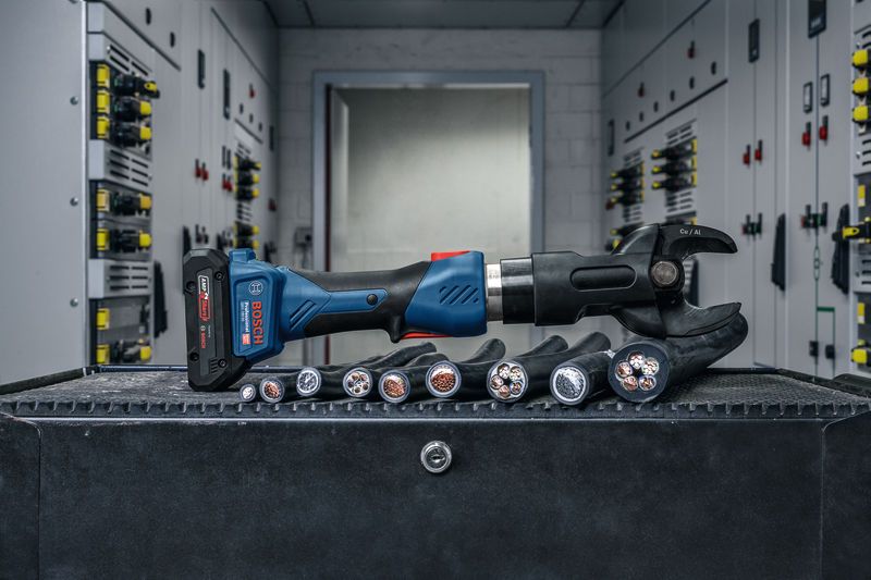 Herramienta de corte hidráulica inalámbrica colocada en un banco de trabajo junto a cables eléctricos gruesos.