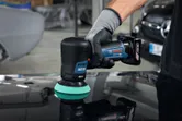 Una persona que usa equipo de seguridad utiliza una pulidora inalámbrica en la superficie de un automóvil.