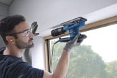Una persona que usa equipo de seguridad lija el marco de una ventana con una lijadora orbital.