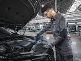 Una persona que usa equipo de seguridad utiliza una herramienta inalámbrica en el motor de un automóvil en una fábrica.