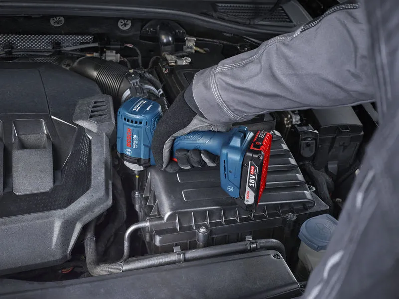 Una persona que usa equipo de seguridad utiliza un destornillador de impacto inalámbrico en el motor de un automóvil.