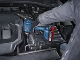 Una persona que usa equipo de seguridad utiliza un destornillador de impacto inalámbrico en el motor de un automóvil.