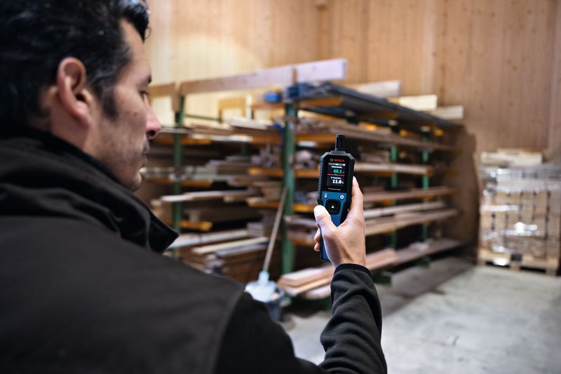 Una persona utiliza un termohigrómetro para medir la temperatura y la humedad en un área de almacenamiento de madera.