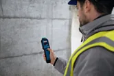 Una persona que usa equipo de seguridad utiliza un medidor de humedad del material para comprobar una pared de hormigón.