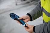 Una persona que usa equipo de seguridad sostiene un medidor de humedad del material en el interior.