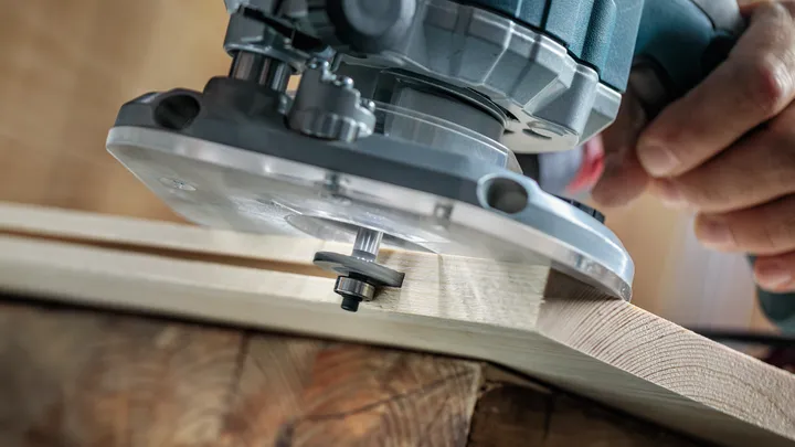 Una persona da forma al borde de una tabla de madera con una fresadora eléctrica.