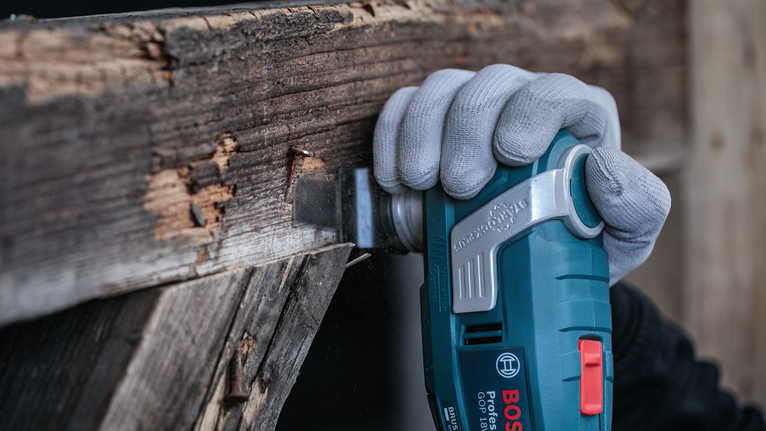 Una persona que usa equipo de seguridad utiliza una herramienta eléctrica para cortar una viga de madera.