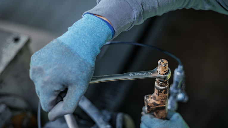 Una persona que lleva puesto un equipo de seguridad aprieta una pieza oxidada con una llave inglesa.