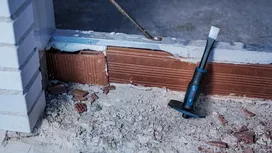 Cincel colocado sobre el polvoriento suelo de una obra en construcción, cerca de un muro de ladrillos parcialmente demolido.