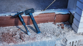 Martillo y cincel de albañilería sobre una superficie de ladrillo polvorienta en una obra en construcción.