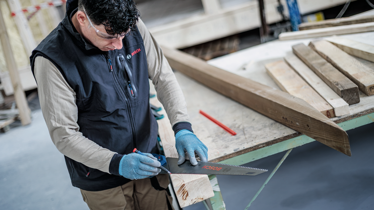 Una persona, equipada con equipo de seguridad, marca una tabla de madera con una sierra sobre un banco de trabajo.