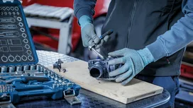 Una persona que lleva puesto un equipo de seguridad utiliza una llave de carraca para reparar una pieza mecánica.