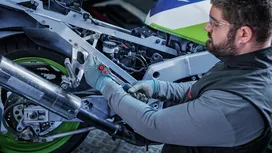 Una persona que lleva puesto un equipo de seguridad utiliza una herramienta eléctrica para apretar un perno en el chasis de una motocicleta.