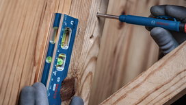 Una persona que lleva equipo de seguridad utiliza un nivel y un destornillador sobre tablas de madera.