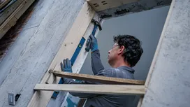 Una persona que lleva equipo de seguridad utiliza un martillo para ajustar el marco de una puerta de madera.