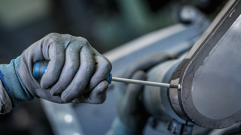 Una persona que lleva puesto un equipo de seguridad aprieta un tornillo en una máquina industrial.