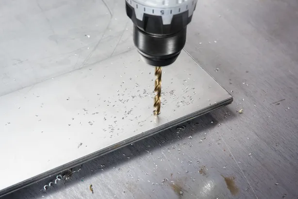 Cordless drill making a hole in a metal sheet, metal shavings scattered around.