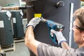 A person wearing safety equipment uses a heat gun to apply a label to a large tank.