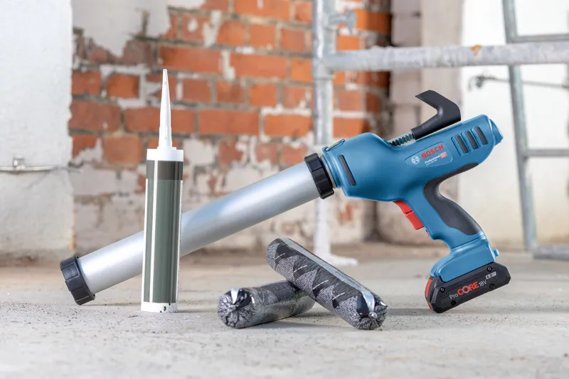 Cordless caulk gun on a concrete floor beside caulk cartridges in a construction area.