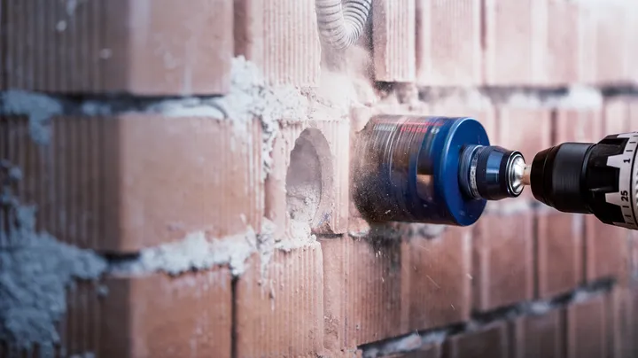 Hole saw attachment drilling a circular opening in a brick wall.