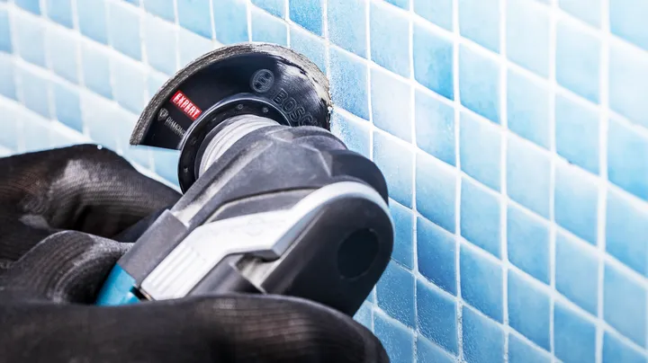 Person wearing safety equipment uses a power tool to cut blue ceramic tiles.