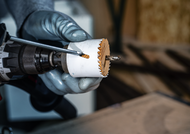 Person wearing safety equipment uses a drill with a hole saw to cut through wood.