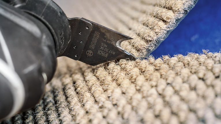 Power tool blade cutting through thick carpet on a blue surface.
