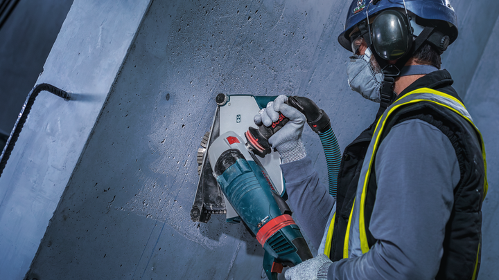 A person wearing safety equipment uses a power tool to cut a concrete wall.