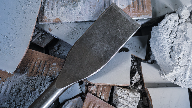 Chisel lying on broken concrete and tile pieces.