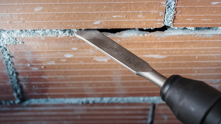 Chisel attachment removing mortar from brick joint.