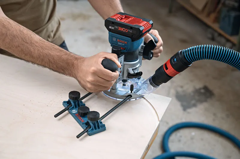 A person guides a cordless palm router along a curved wooden edge in a workshop.
