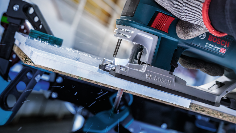 Person wearing safety equipment cuts a plastic sheet with a jigsaw.