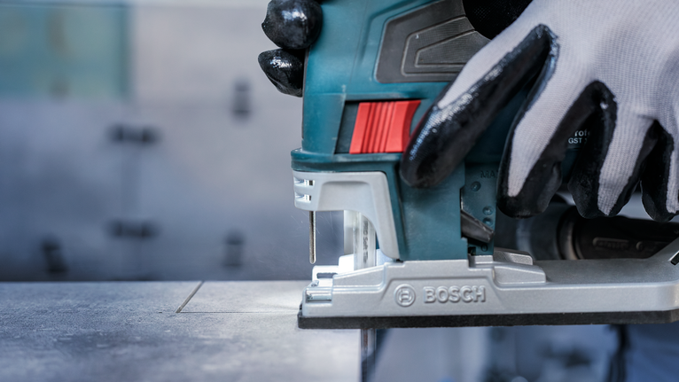 Person wearing safety equipment uses a jigsaw to cut a straight line in a metal sheet.