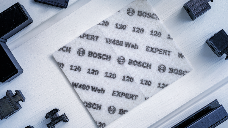 A white abrasive sanding sheet with printed specifications is placed on a light wooden surface.