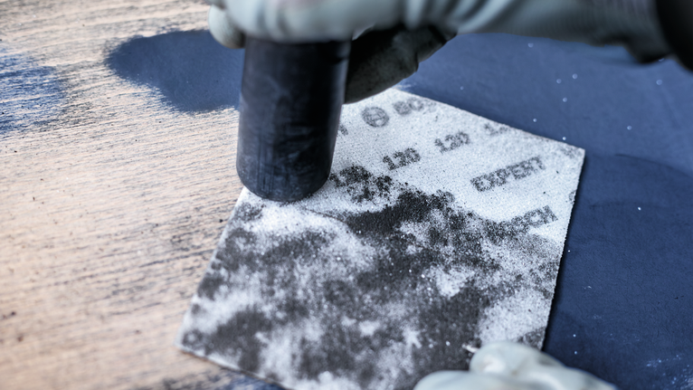 Person wearing safety equipment sanding a wooden surface with a sanding block.