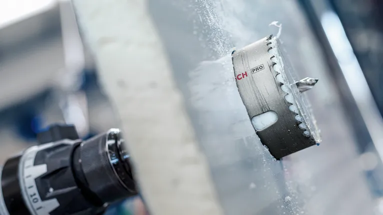 Hole saw attachment drilling through a thick glass panel.
