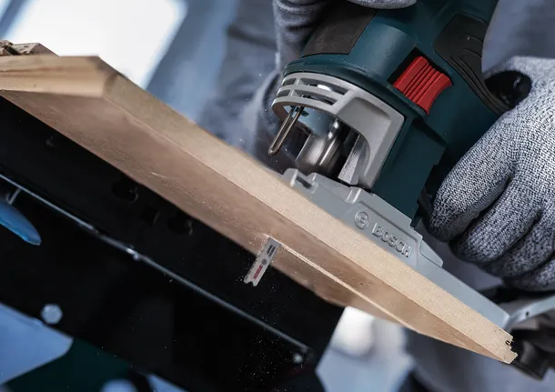 Person wearing safety equipment uses a jigsaw to cut a wooden board.