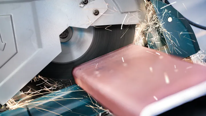 Sparks fly as a chop saw blade cuts through a metal bar.