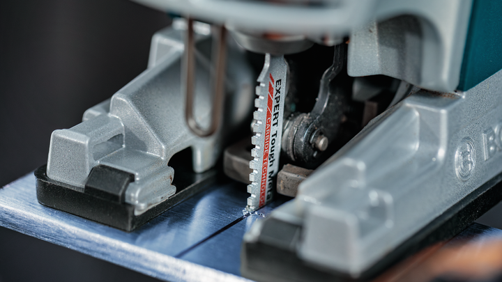 Close-up of a jigsaw blade cutting through a sheet of metal.