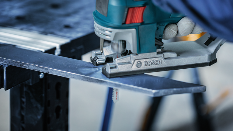 Person wearing safety equipment cuts a metal plate with a jigsaw.