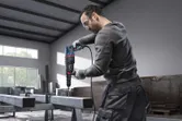A person wearing safety equipment drills into a steel beam with a rotary hammer.