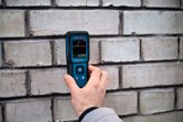 A person measures wall moisture using a material moisture meter.