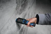 A person measures wall moisture using a material moisture meter.