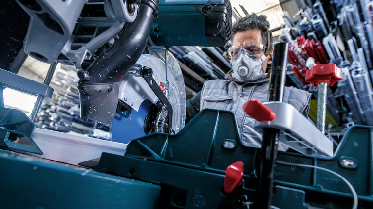 Person wearing safety equipment operates a circular saw in a workshop.