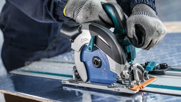 Person wearing safety equipment guides a circular saw to cut a sheet of metal.