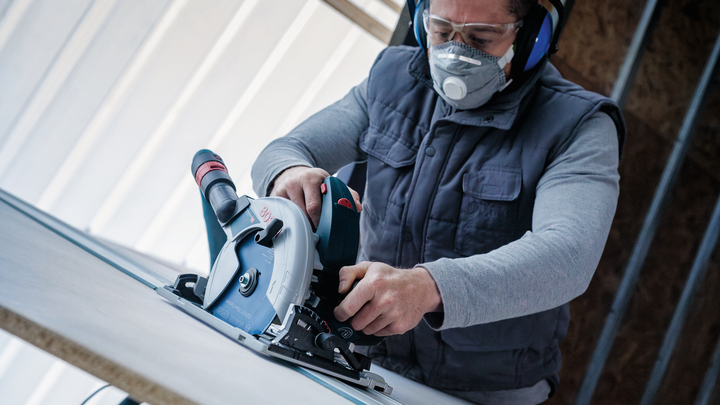 Person wearing safety equipment uses a circular saw to cut a board.